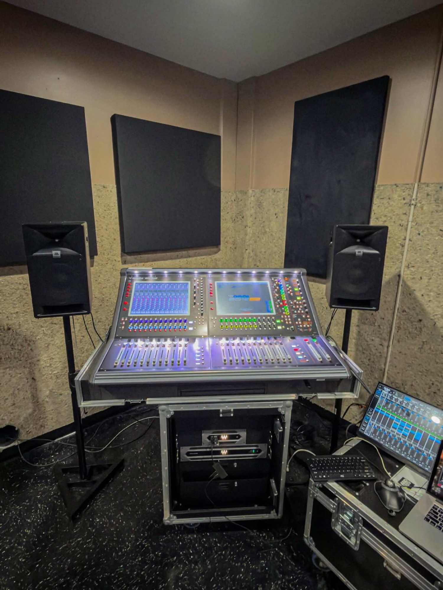 A DiGiCo console glowing purple in a small treated control room flanked by studio monitors on stands.