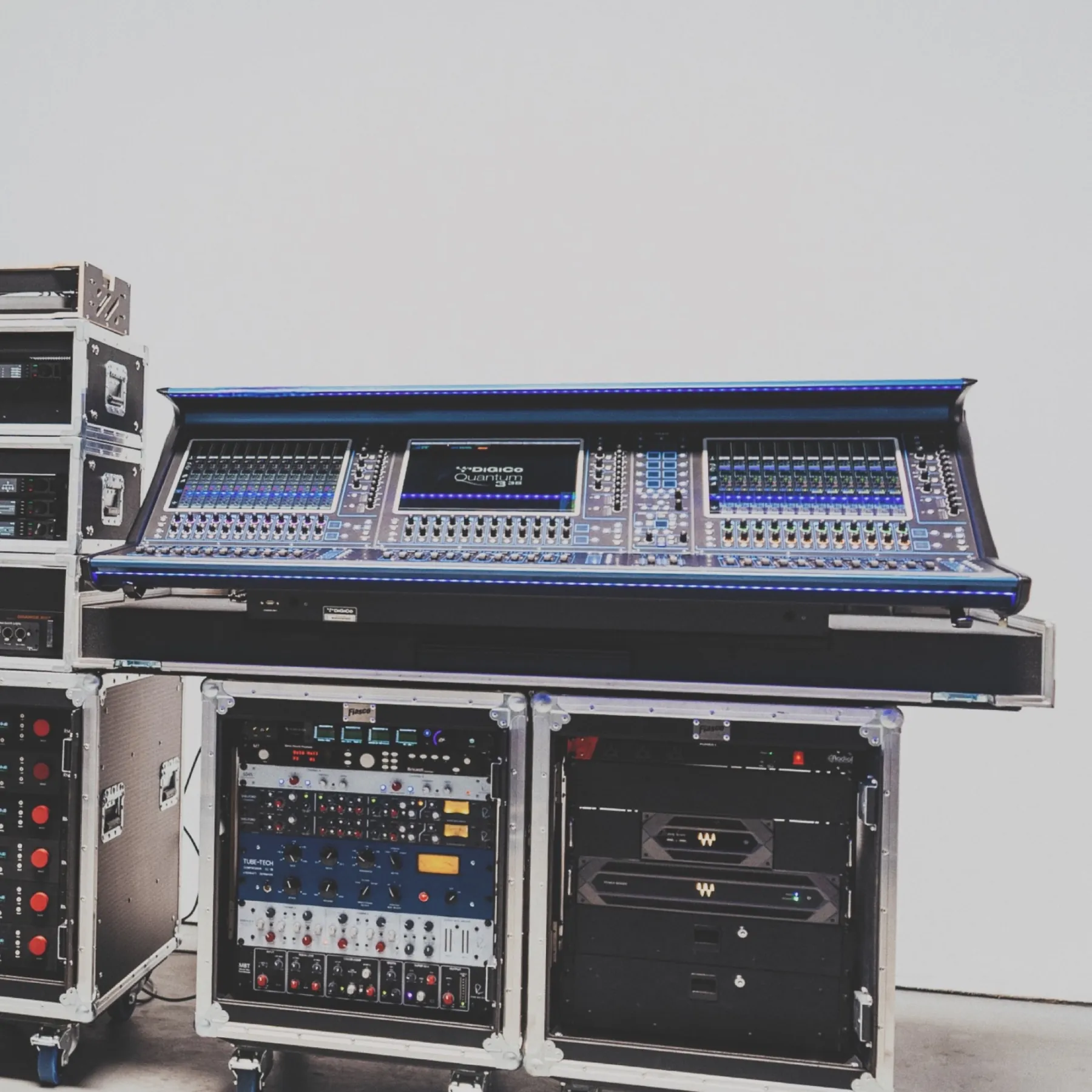 A blue DiGiCo Quantum console on flight cases with a Waves SoundGrid rack drawer open, on a clean white studio backdrop.