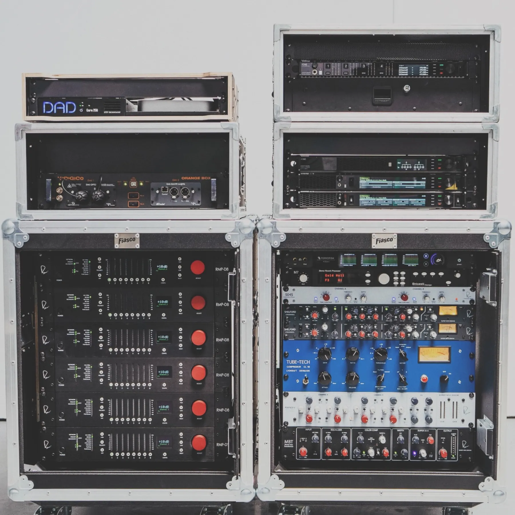 Two flight-cased racks against white: a stack of power amplifiers beside a rack of premium outboard gear including Rupert Neve, Tube-Tech and Bricasti units.