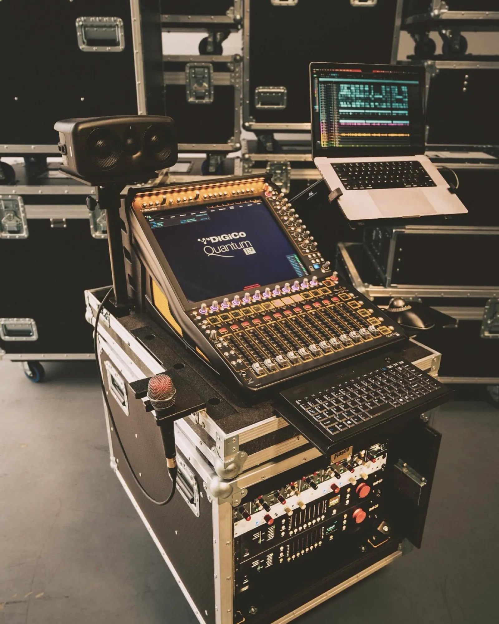 A DiGiCo Quantum on a rolling rack cart with a laptop, talkback mic and keyboard, staged among road cases in the warehouse.