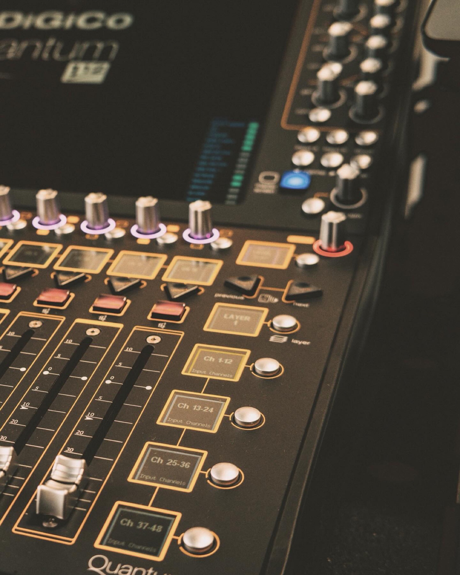 A close-up of a DiGiCo Quantum 338 control surface with gold-trimmed faders, encoders and channel screens.