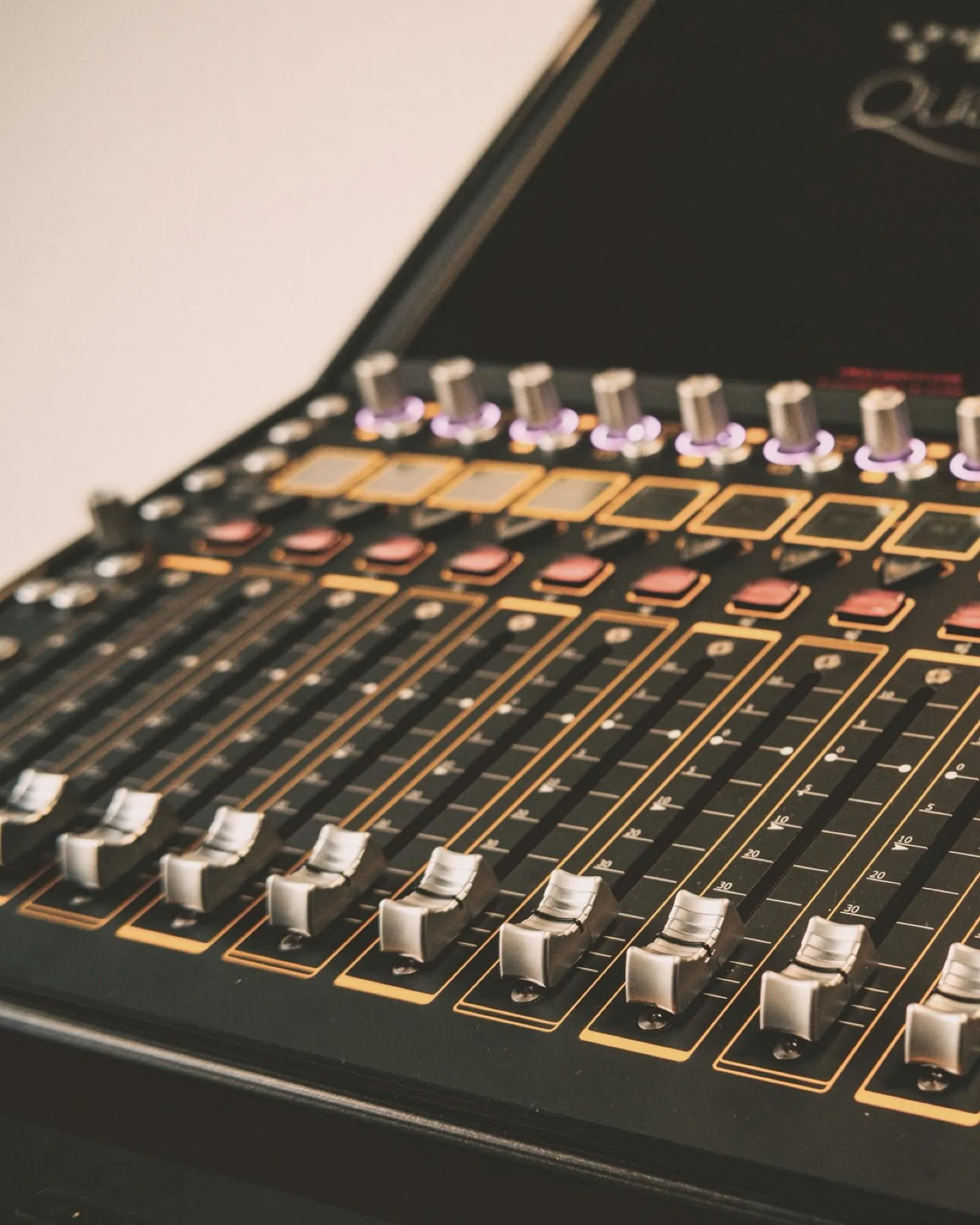 An angled macro of a console's gold-and-black fader bank with shallow depth of field.